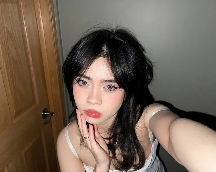 Menina oriental com lentes azuis nos olhos e corte de cabelo preto wolf cut. Ela tira selfie em fundo de parede com porta