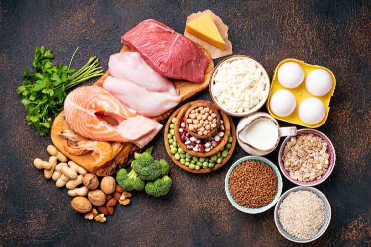 A imagem apresenta uma variedade de alimentos ricos em proteínas dispostos sobre uma superfície escura. Os alimentos incluem diferentes tipos de carne, laticínios e leguminosas, representando uma seleção diversificada de fontes de proteína, eles funcionam melhor que termogênico para acelerar o metabolismo