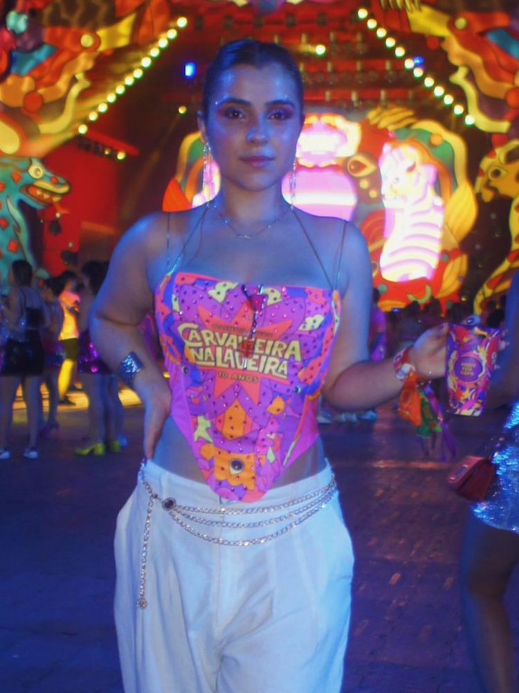 Mulher de pele clara usando abadá rosa customizado em corset e calça branca com correntes