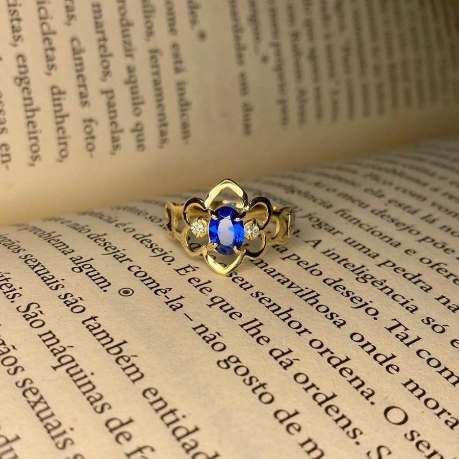 Anel de formatura pedagogia com pedra safira azul, dentro de um livro