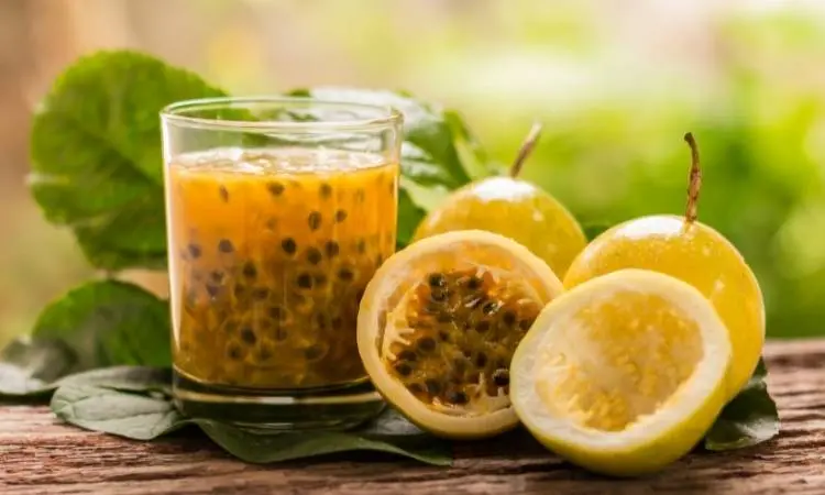 Copo com polpa de maracujá e maracujás cortados ao meio do lado.