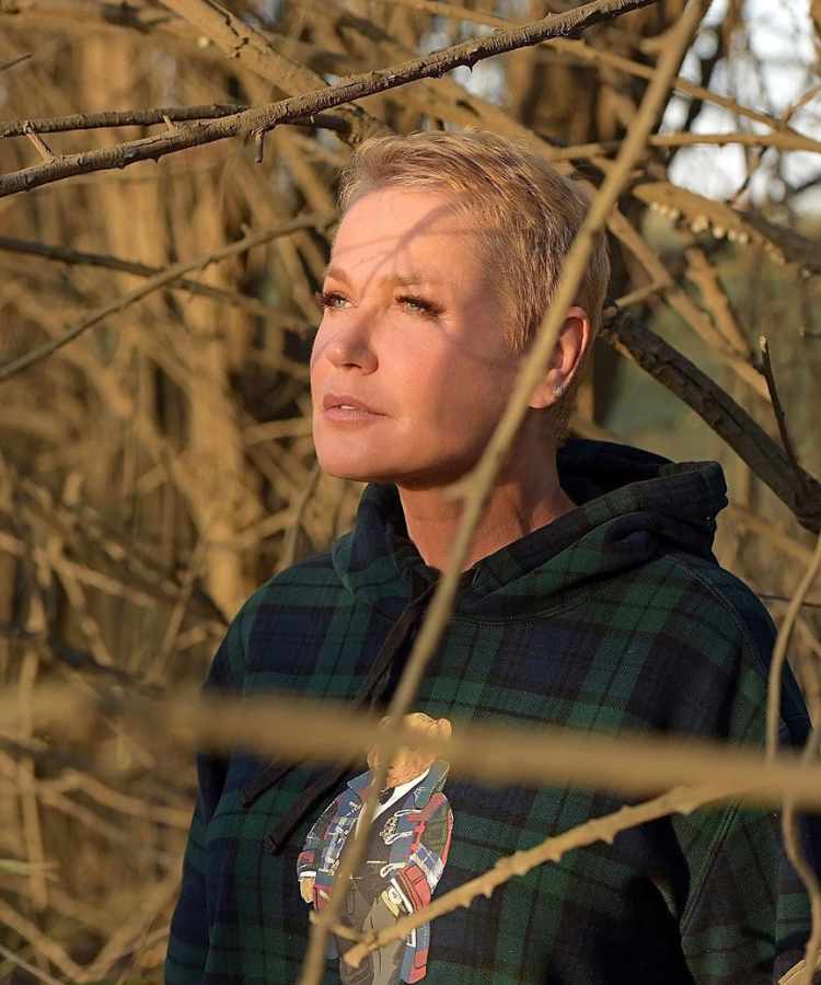 Xuxa em foto distraída em meio a árvores com galhos secos.