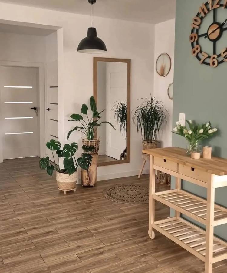 Hall de entrada com decoração Feng Shui, destacando plantas vivas em vasos de fibra natural, espelho grande que reflete energia positiva e uma mesa de madeira clara organizada. Piso de tonalidade quente e iluminação sutil criam harmonia e bem-estar.





