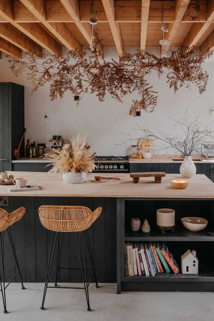 Cozinha em tons de preto e madeira, com velas, vasos, folhas secas e decorações