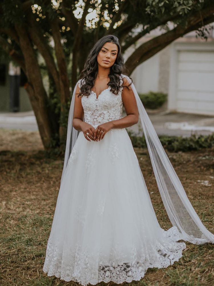 Mulher de pele negra usando vestido de noiva bordado e capa nos dois ombros