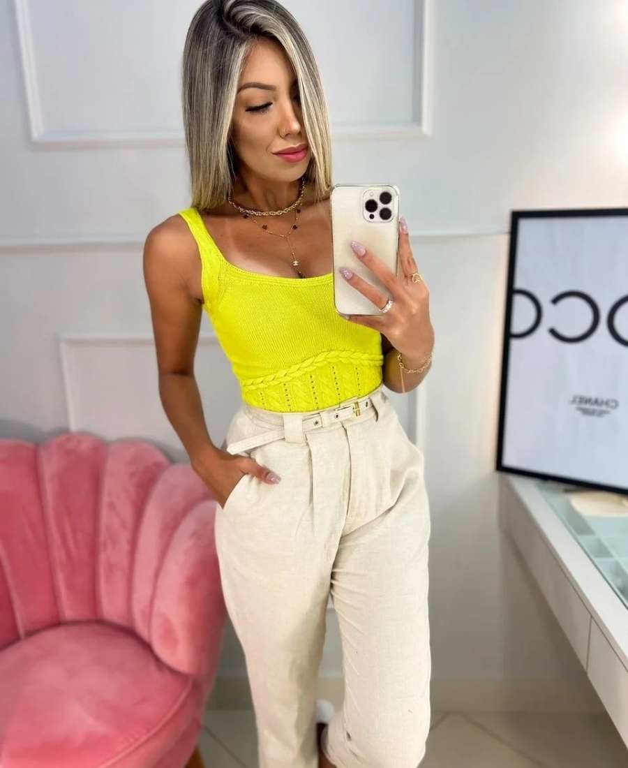 Imagem com fundo de parede com sofá rosa. No centro, mulher usando roupas amarela: camiseta amarela + calça off white.