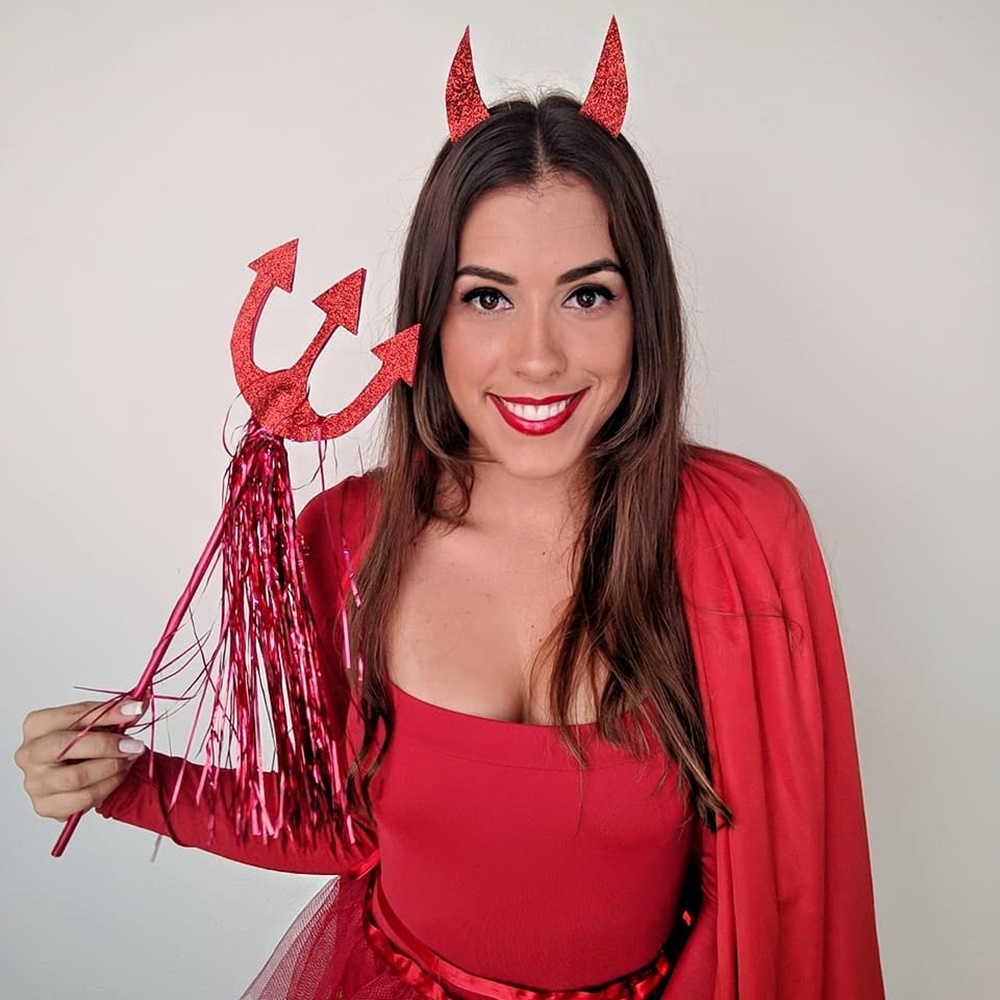 Mulher de pele clara com fantasia vermelha, tiara de diabinha vermelha e tridente