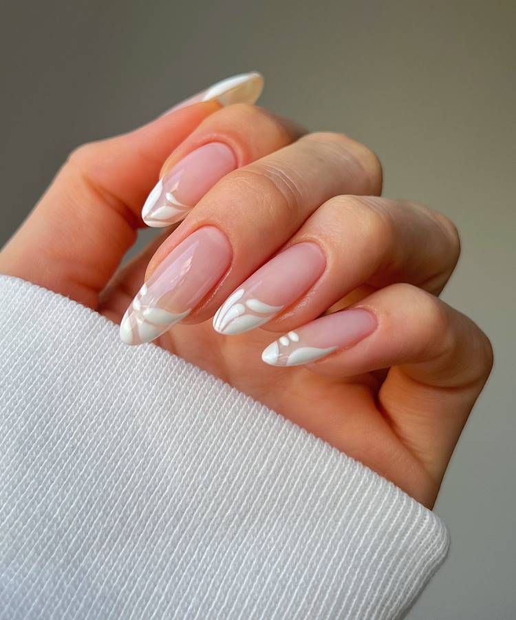 Mãos femininas com unhas em formato oval, decoradas com esmalte perolado e detalhes dourados minimalistas. Anéis delicados, incluindo um com pedra central, complementam o visual elegante. O fundo neutro realça a sofisticação e o brilho das unhas.





