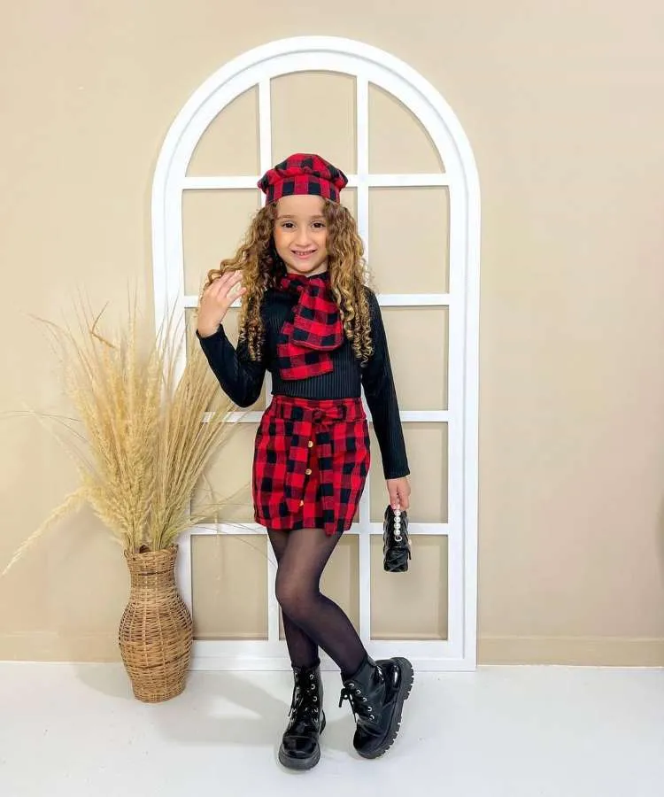 Menino usando look country preto com saia, boina e lenço xadrez vermelho.
