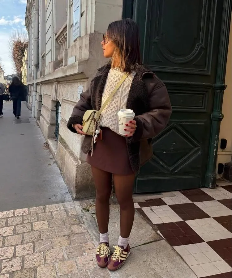 Mulher usando look com meia-calça, suéter, shorts saia e tênis