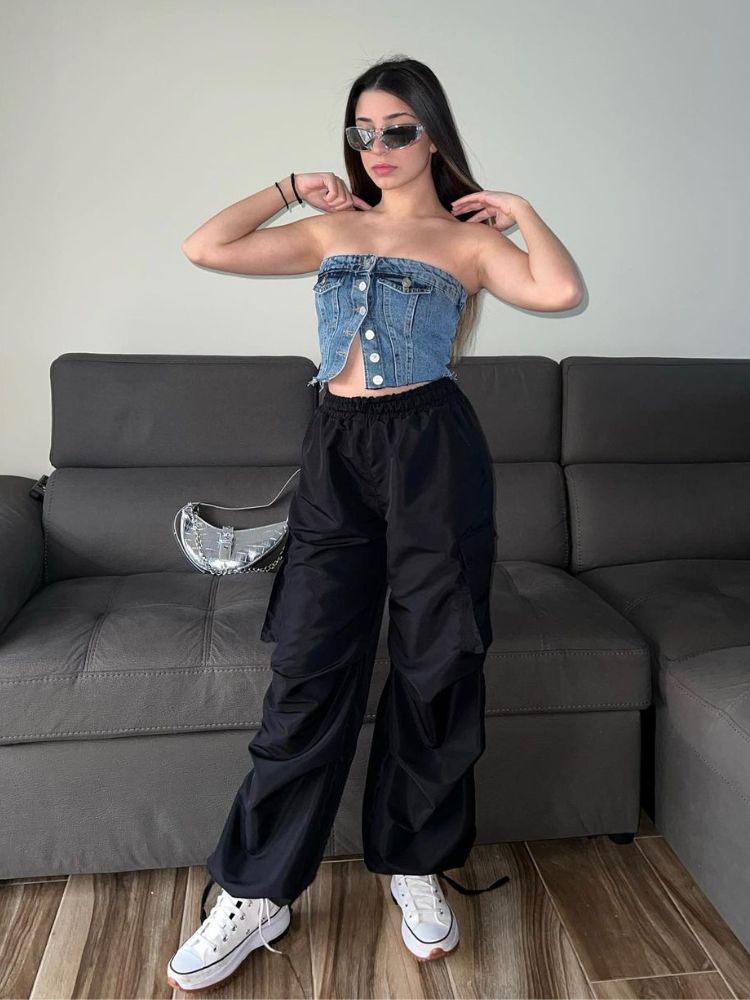 Mulher de pele clara usando parachutes pants preta, cropped jeans, all star branco e óculos espelhados. 