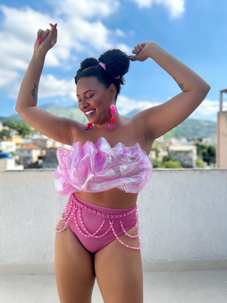 Mulher de pele negra com look rosa de top de tule e hot pant com body chaim de miçanga 
