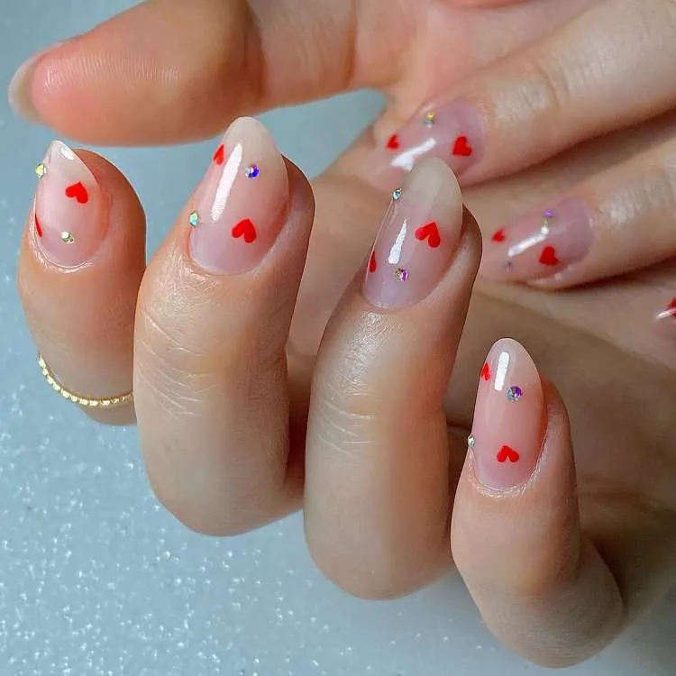 Unhas cor natural decoradas com corações de cor vermelha e pedrinhas
