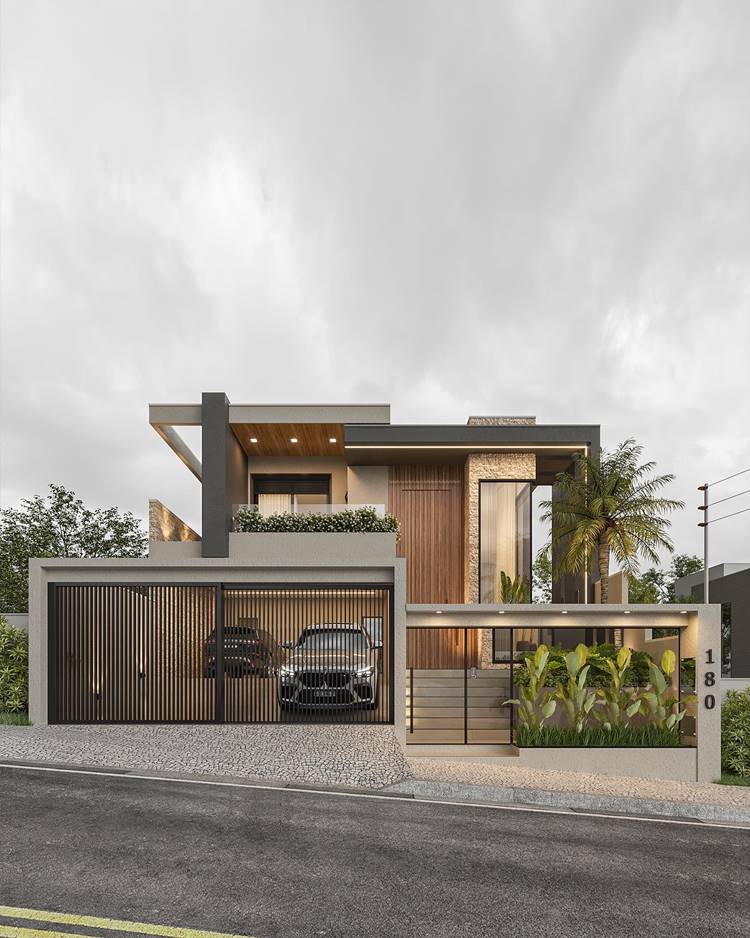A imagem mostra uma casa moderna de dois andares com um design arquitetônico contemporâneo. O exterior da casa é uma combinação de concreto cinza claro e painéis de madeira. Há uma garagem coberta à esquerda com portões verticais de ferro e vidro. A entrada principal está à direita, destacada por uma porta de madeira alta e iluminação suave. O segundo andar possui uma varanda com guarda-corpo de vidro e plantas que adicionam um toque verde ao design geral. O céu está nublado, proporcionando uma iluminação suave que realça os detalhes arquitetônicos da casa.
