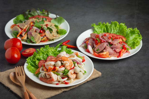 Mesa preta com três pratos de saladas com frutos do mar, tomate e alface 