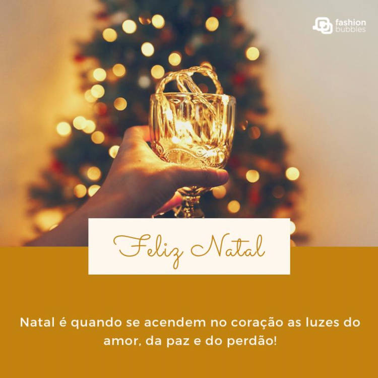 Foto de mão segurando cálice perto de árvore natalina e frase: Natal é quando se acendem no coração as luzes do amor, da paz e do perdão!