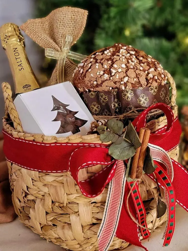 Foto de cesta de vime de Natal com laços, panetone, champanhe e caixa branca com doces 