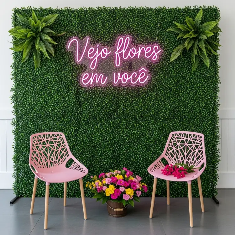 Uma parede coberta por folhagem artificial e decorada com flores falsas. Na frente, duas cadeiras rosas com pernas de madeira. Entre elas, um balde de flores. Acima, um letreiro de neon rosa diz "Vejo flores em você".







