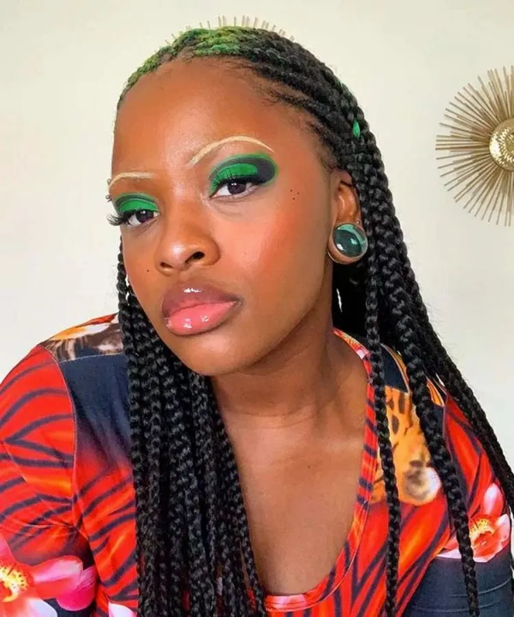 Mulher negra com trança nagô, maquiagem verde nos olhos e roupa colorida