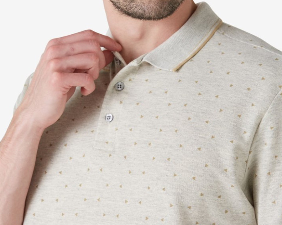 Homem de pele clara usando camisa polo bege com triângulos