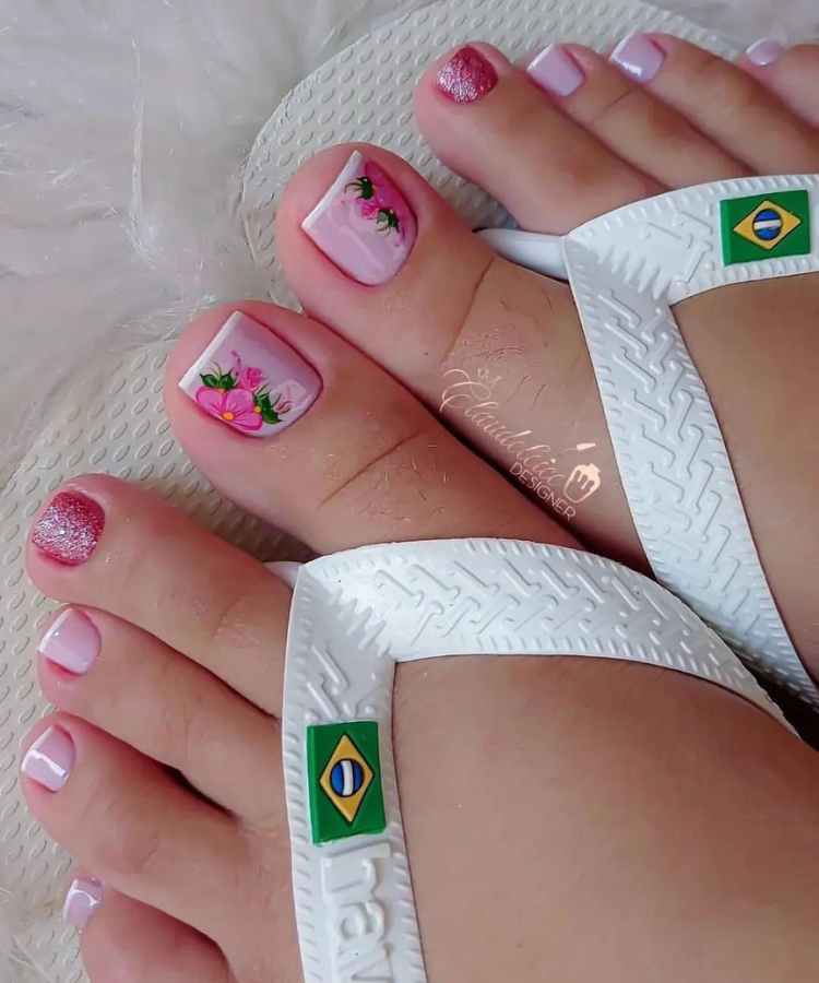 Pé de pessoa de pele clara usando chinelo branco e unhas francesinha com adesivo de flor rosa e unhas rosa com glitter