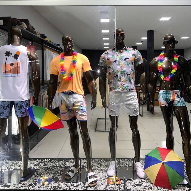 Vitrine carnavalesca de loja de roupas masculinas, com manequins vestidos, com colar havaiano e guarda-chuva de frevo