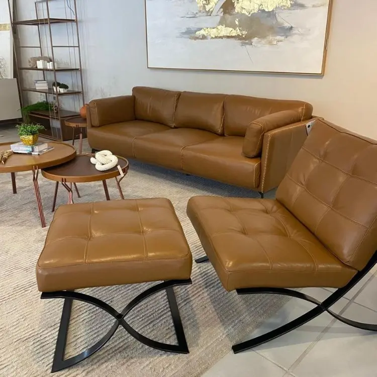 Sala com sofá, aparadores redondos e poltronas em couro marrom, com tapete bege e quadro grande na parede