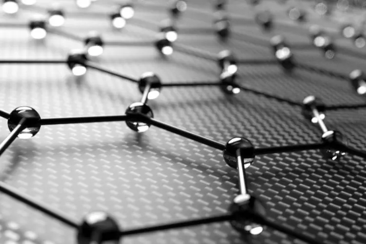 Esta imagem em preto e branco mostra uma representação 3D de uma estrutura molecular de grafeno. Pequenas esferas interligadas por hastes formam uma malha hexagonal, simbolizando os átomos de carbono.