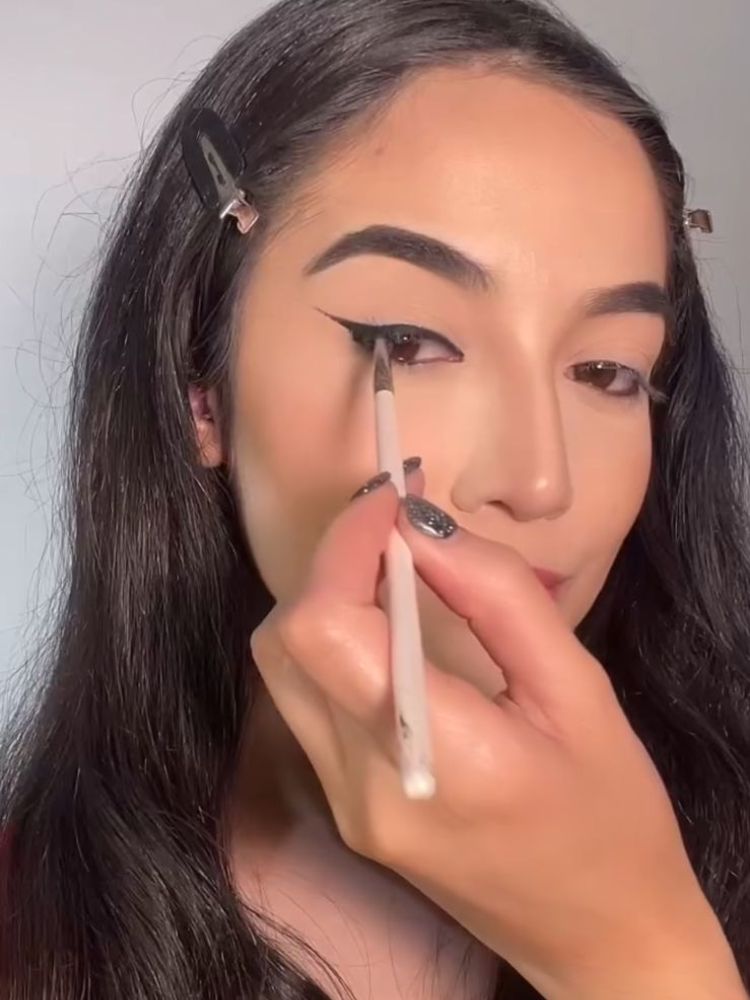 Mulher de pele clara fazendo delineado gatinho preto com pincel 