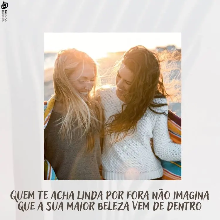 Foto de duas amigas sorrindo uma para a outra. Uma delas tem cabelo loiro e está de blusa cinza e a outra tem cabelo escuro e usa uma blusa branca. Abaixo da foto, há a frase "Quem te acha linda por fora não imagina que a sua maior beleza vem de dentro". 