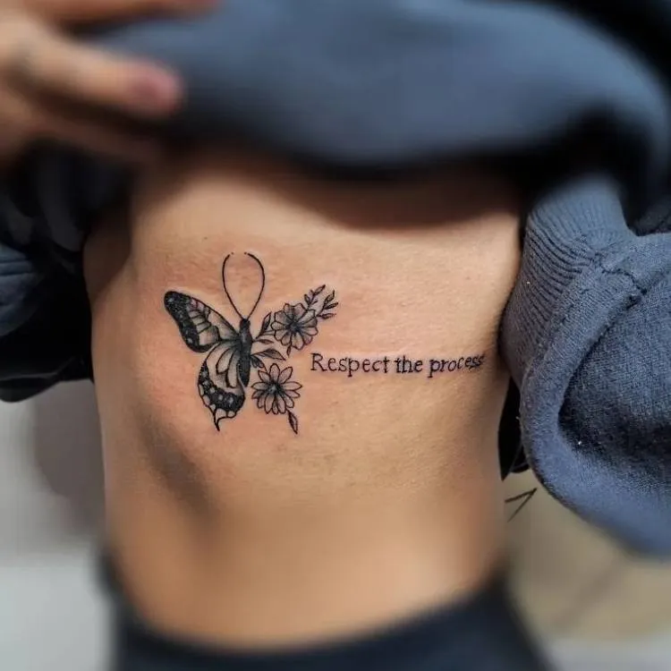 Ttuagem grande de borboleta com traços finos e grossos, flores e frase "respect the process" na costela de uma mulher de pele clara. 