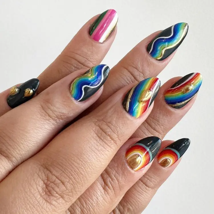 Unhas de fundo preto com nails arts em cores do arco-íris e detalhes em 3D dourado 