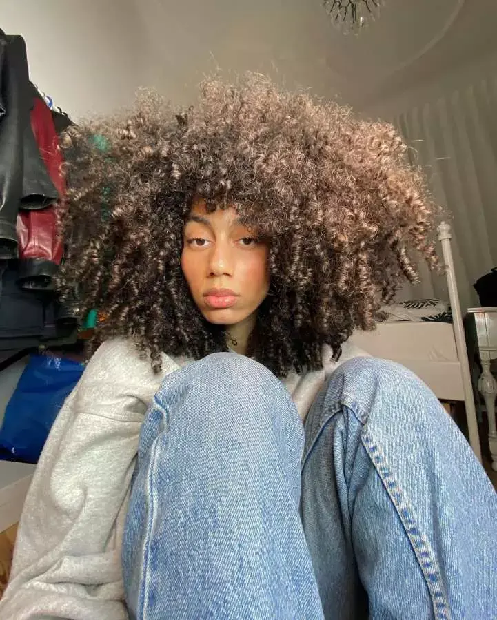 Mulher com corte de cabelo médio crespo franja irregular