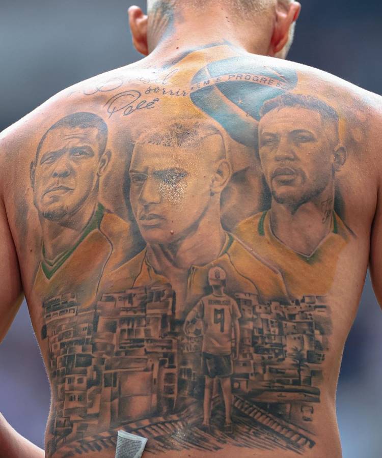 Costas de Richarlisson tatuadas com ilustrações detalhadas: retratos de jogadores de futebol, incluindo Richarlison, e a imagem de uma criança em uma favela vestindo uma camisa com o número 9, representando superação e ligação ao esporte brasileiro.





