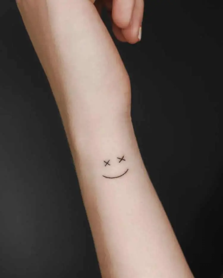 Pulso lateral tatuado com carinha feliz, sendo os olhos dois "x"