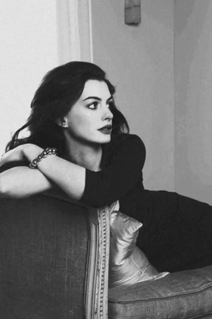 Frase para foto pensativa Anne Hathaway sentada no sofá, veste vestido preto e usa pulseira