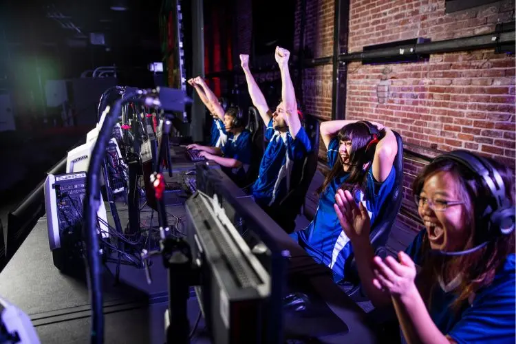 5 pessoas sentadas em frente a seus computadores comemorando vitória em esportes eletrônicos