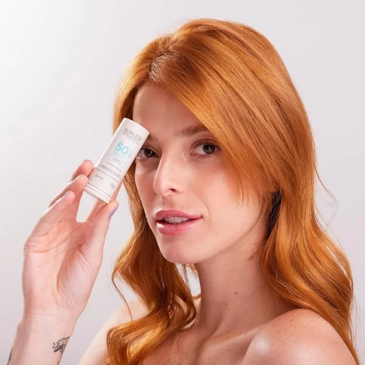 Foto de mulher ruiva segurando protetor solar em bastão com cor da Sunless