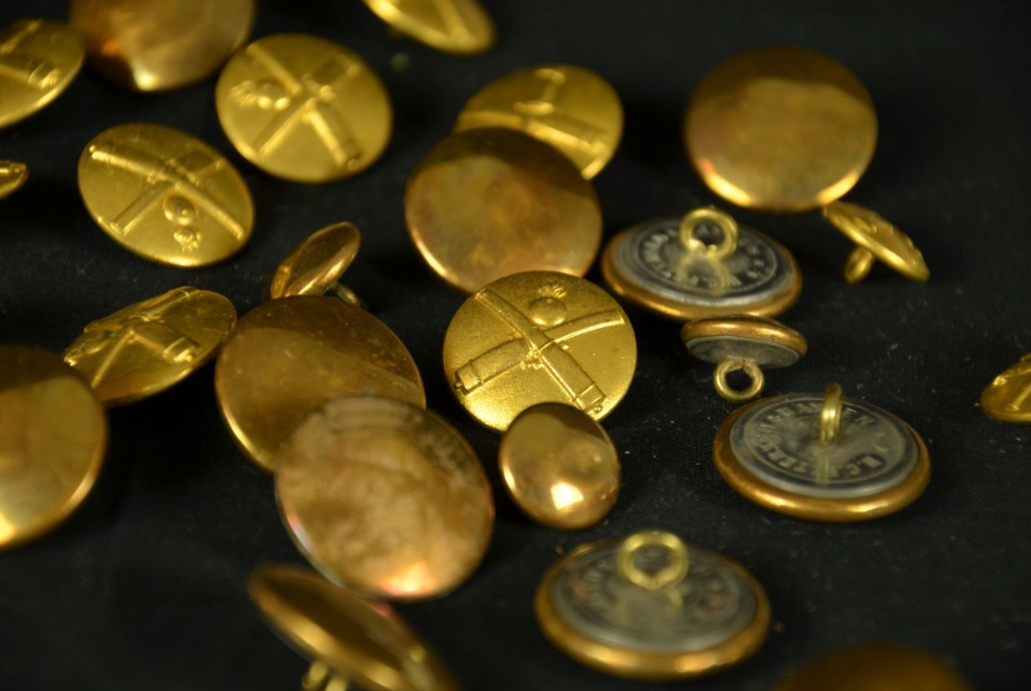 Imagem de vários botões de bronze decorado com um desenho em relevo de armas cruzadas sobre fundo preto