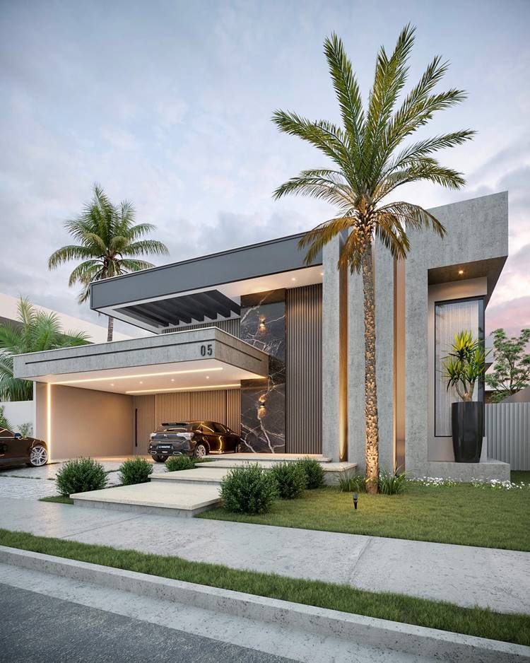 Fachada de casa moderna, com design angular, paredes de concreto cinza e grandes janelas. Há uma garagem aberta e um jardim bem cuidado na frente. A casa tem iluminação interna que a destaca contra o céu escuro. O número da casa é “05”