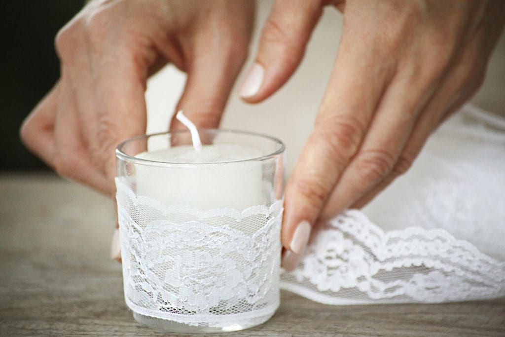 Pessoa de pele clara colocando renda ao redor de recipiente com vela