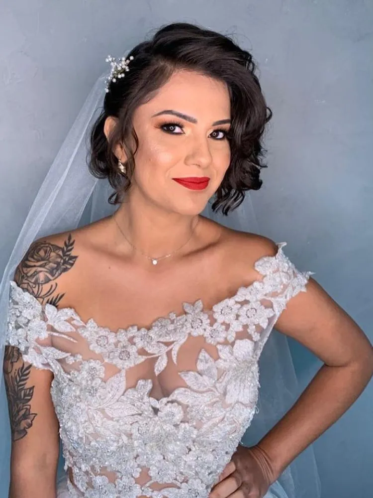 Mulher de pele clara usando vestido de noiva rendado, véu e cabelo curto 