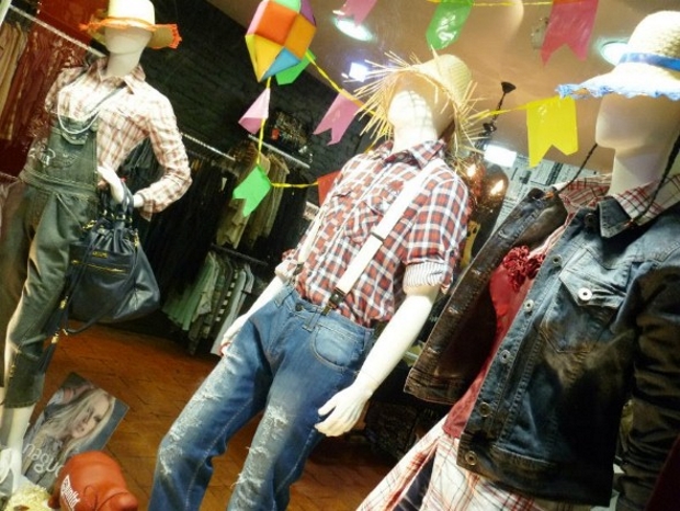 Vitrine com roupas xadrez, bandeirinhas, balões, chapéus de palha