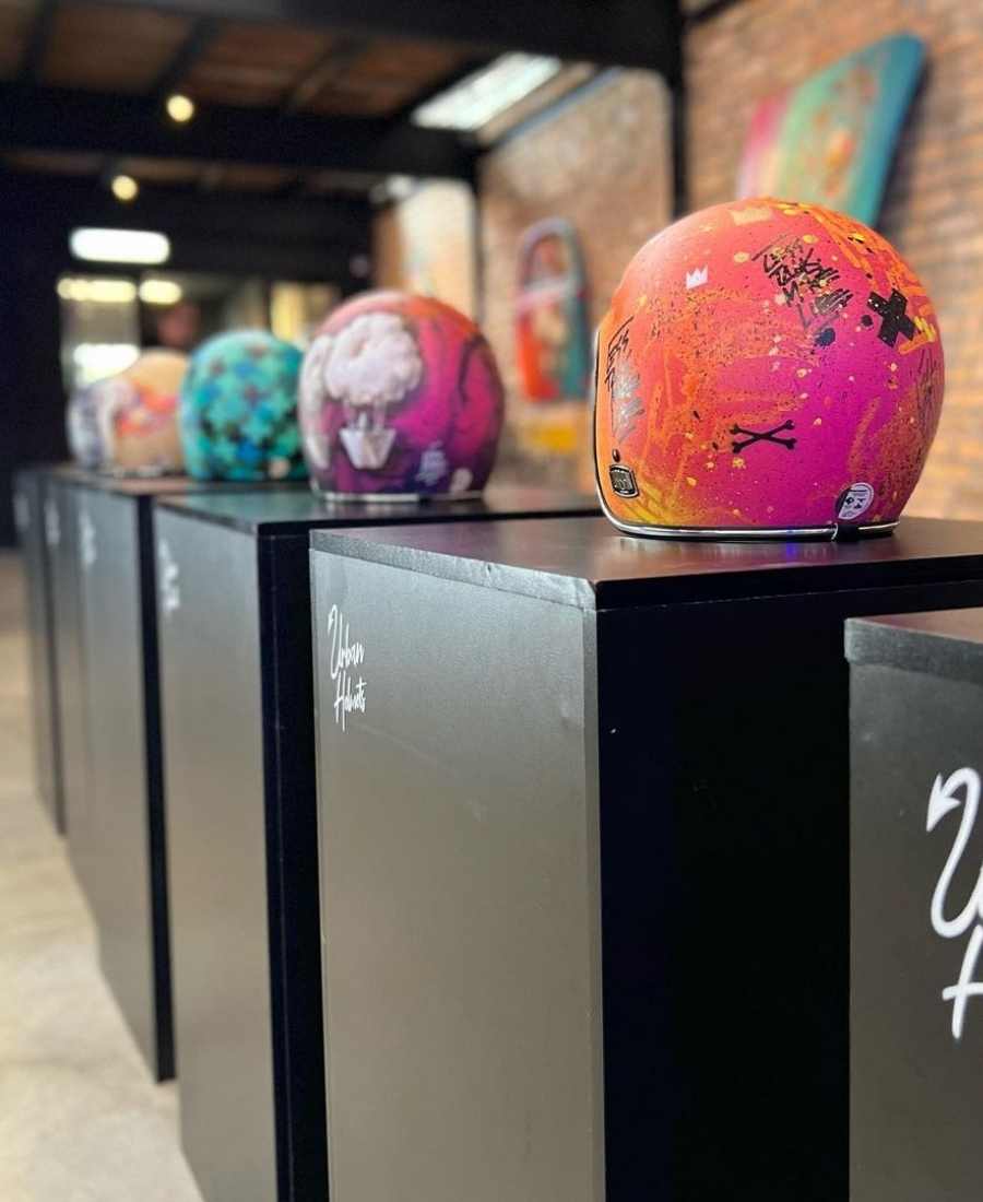 Foto de capacetes coloridos da nova coleção da Urban Helmets. Arte neles com cores rosa, roxo, laranja, amarelo, branco, preto, azul e verde.