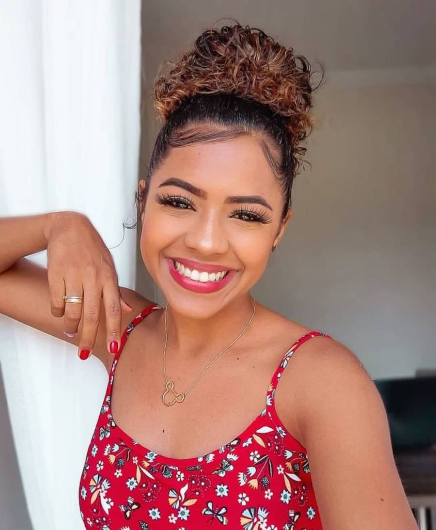 Mulher de pele morena usando blusa vermelha e cabelo castanho em coque abacaxi
