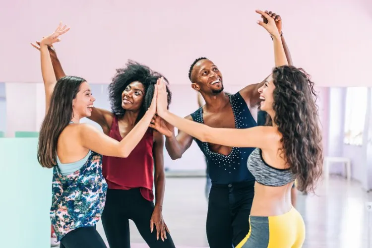 Grupo de 4 pessoas com as mãos unidas sorrindo em salão de dança
