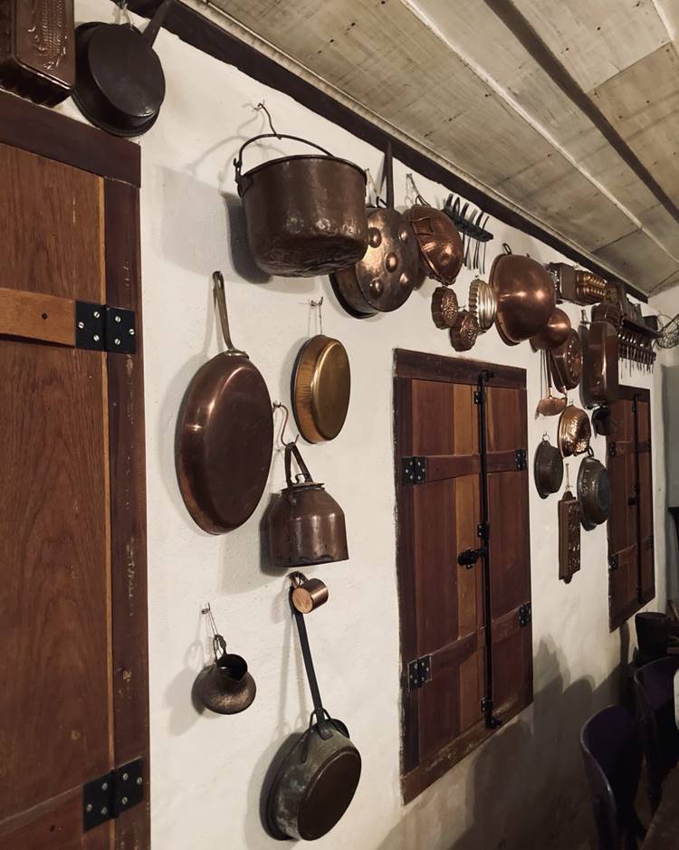 Panelas de cobre penduradas em uma parede com janelas de madeira