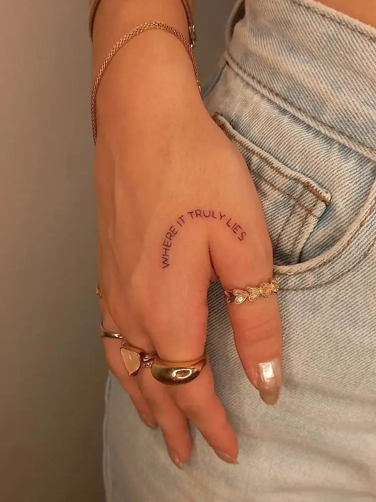 Mão com tatuagem de frase em fineline curva 