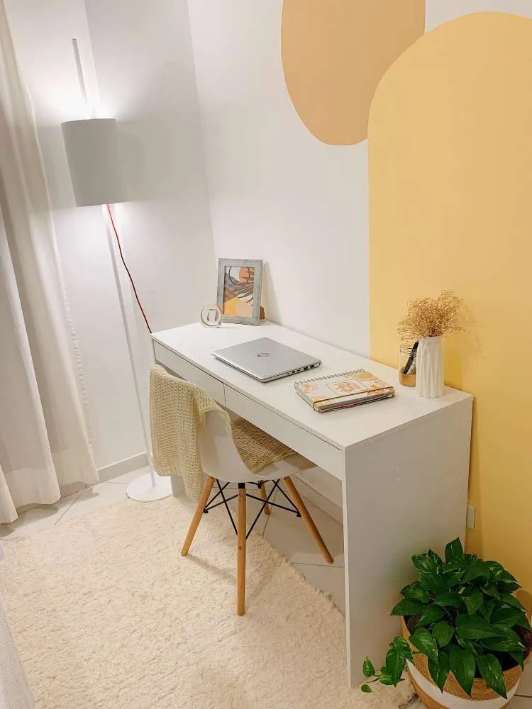 Home office em tons de branco e laranja, com mesa branca, computador, tapete e cestinho com jiboia.