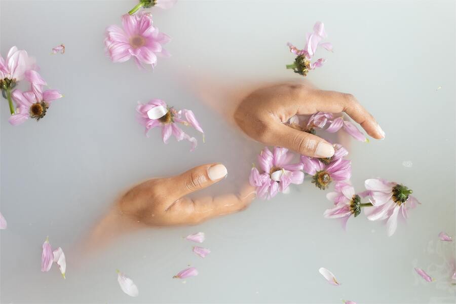 Mãos de pessoa de pele negra em uma banheira com flores roxas para um banho especial com função de simpatia para o amor